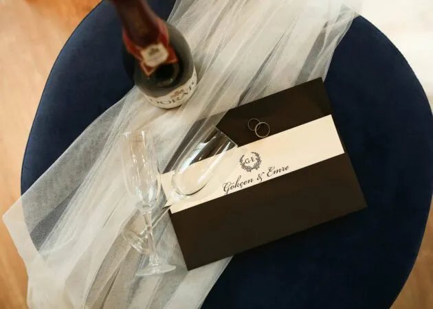 Wedding invitation, champagne glasses, and a bottle arranged on a navy chair with a bridal veil